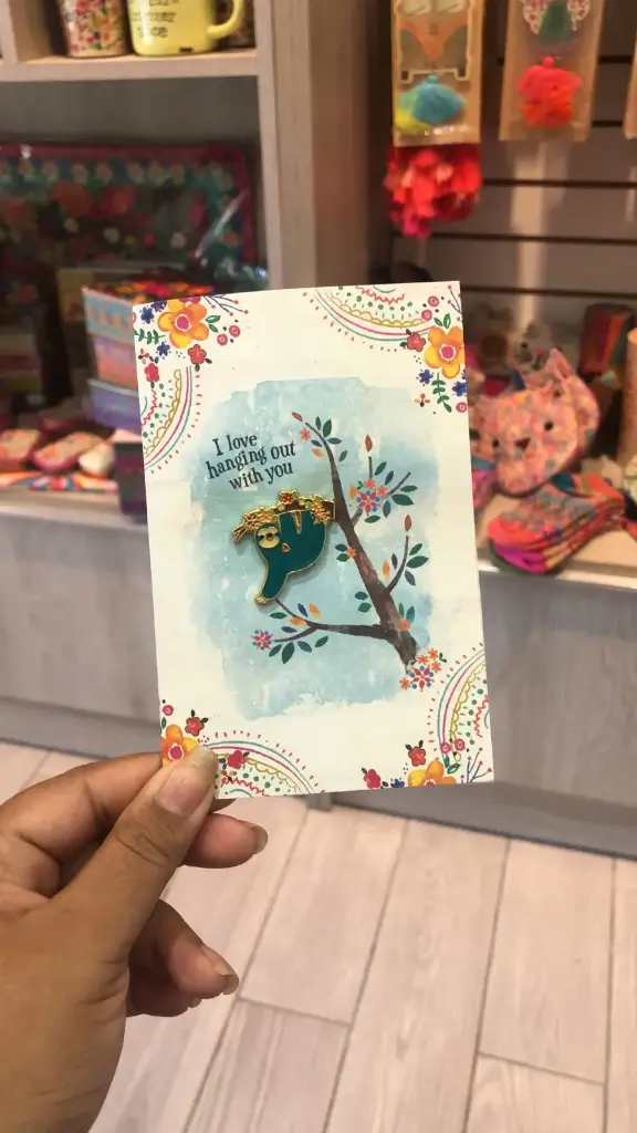 Tarjeta con pin de esmalte de un perezoso colgado